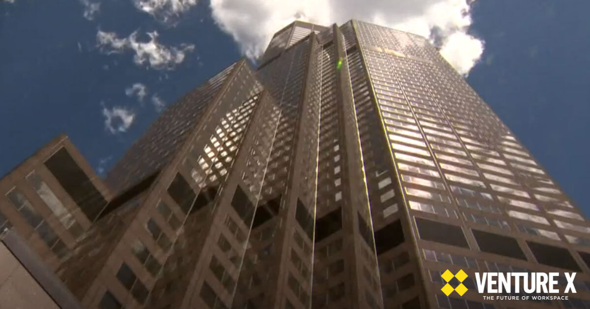 Upward view of a tall office skyscraper against a blue sky, with the Venture X logo in the bottom right corner, symbolizing innovative solutions like virtual offices and flexible workspaces.