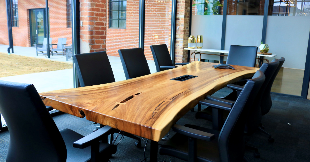 A modern conference room, ideal for a dynamic office space, features a large wooden table surrounded by black chairs. Brick walls and expansive windows enhance the ambiance, creating an inviting atmosphere for collaboration and fostering a vibrant coworking community.
