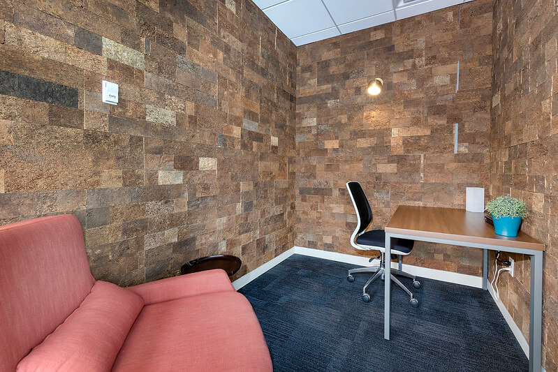 Small modern office space with a pink couch, wooden desk, and black office chair, featuring stone-textured walls.