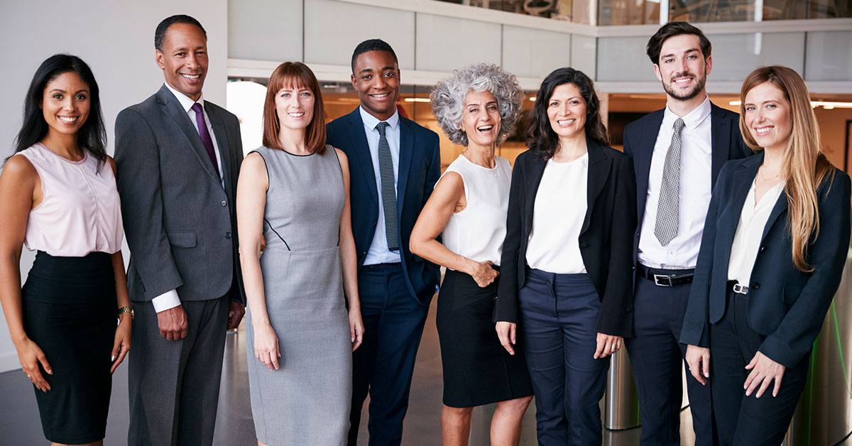 A diverse group of eight professionals stands in a modern coworking space