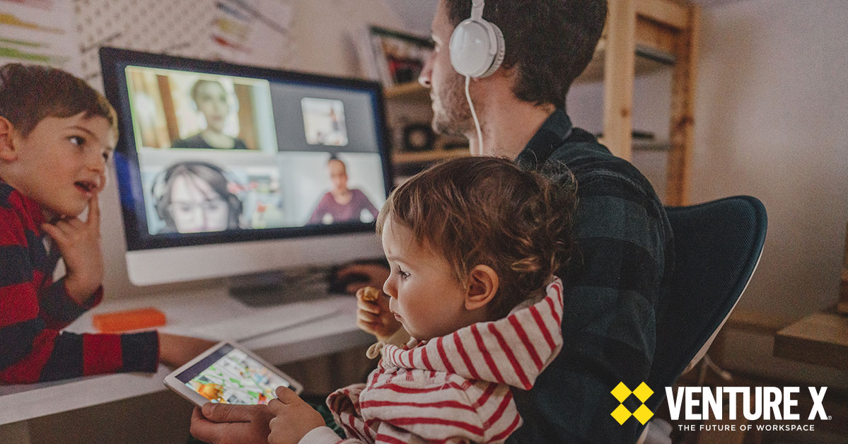 A man wearing headphones sits at a computer in a flexible workspace on a video call