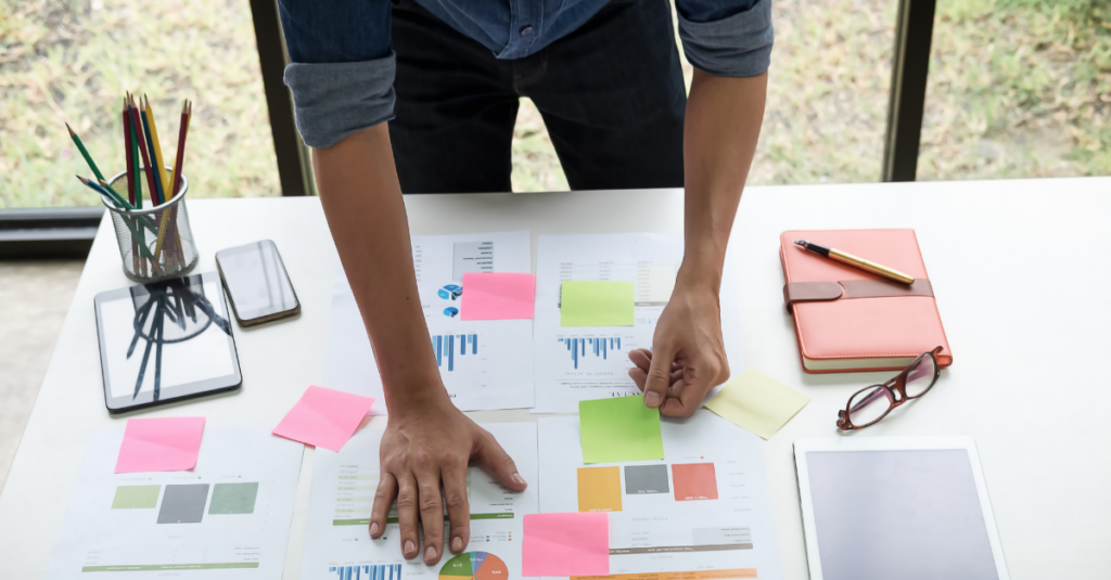 Entrepreneur planning their side hustle on a table with graphs, sticky notes, paper, and a tablet.